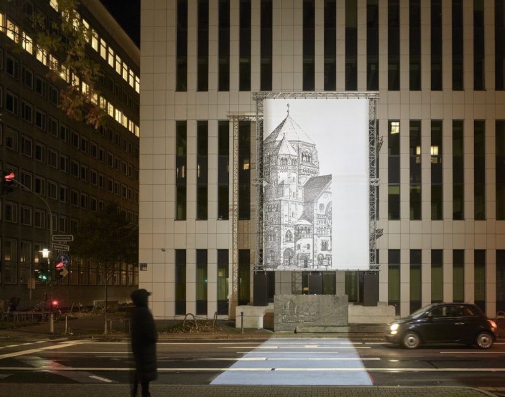 'missing link_': Mischa Kuball secured „that the section of road in front of the memorial stone is brightly lit. A spotlight shines across the street onto a large banner hanging in front of the façade of the new building. It shows a large image of the old synagogue
